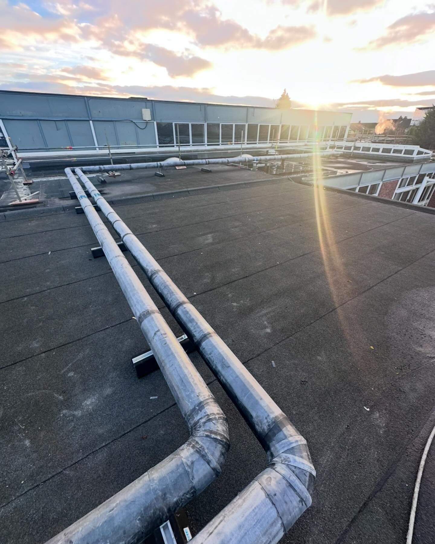 Stainless steel heating pipework running across a school roof at sunset