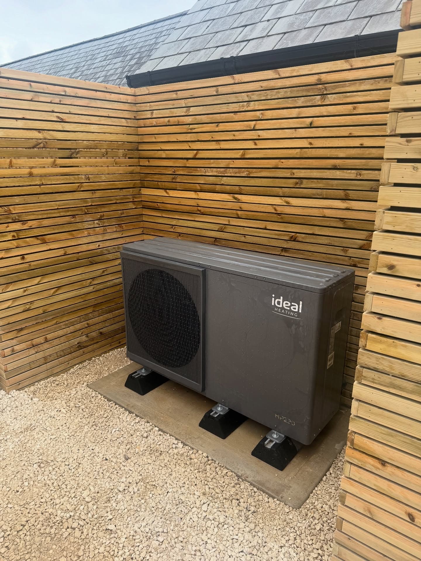 Ideal HP290 air source heat pump installed on gravel against a timber slat wall