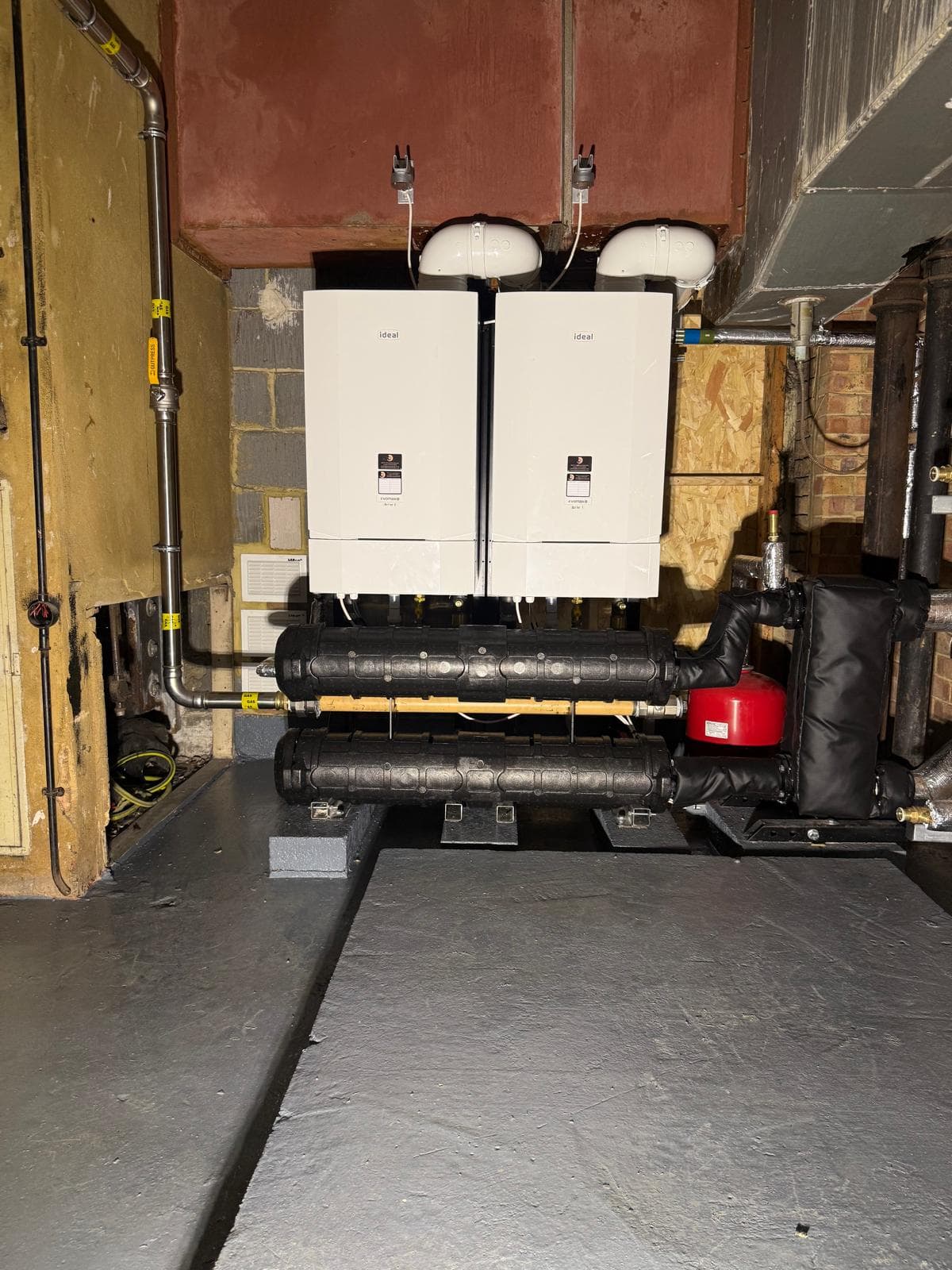 Two Ideal Evomax boilers in cascade with black insulated headers on a painted plinth